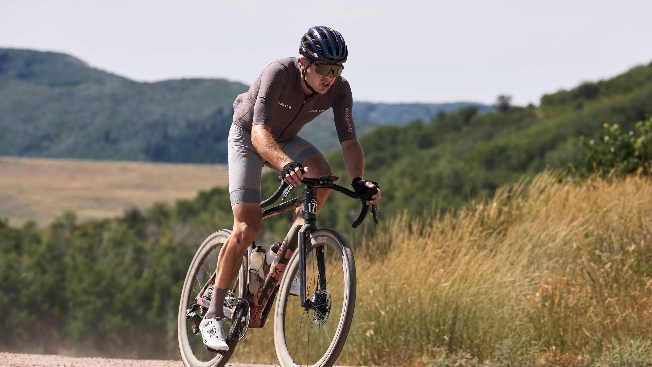 砾石车骑手在尘土飞扬的林道上骑行，配件安装妥当，展示着适合越野探险的装备