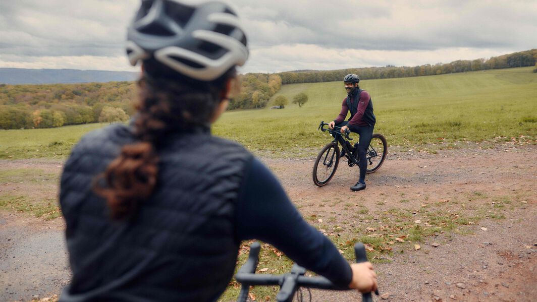 Two cyclists on gravel bikes pause on a dirt trail in the countryside, highlighting different setups and riding postures—ideal for illustrating gravel bike choices.