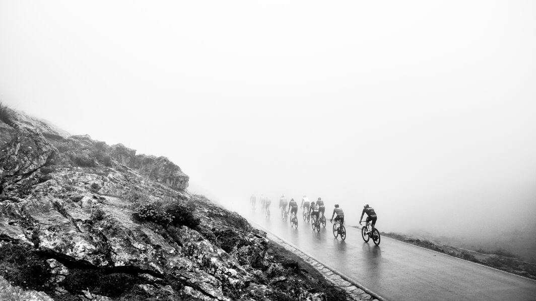 Cyclists riding through dense fog on a steep mountain road during La Vuelta a España, surrounded by rocky terrain and low visibility.